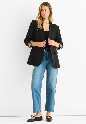 Black blazer with leopard print cuffs, single-button closure, two front pockets. Paired with high-waisted blue jeans and black ballet flats.