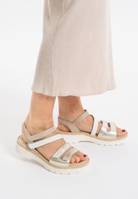 Tan and silver strappy sandals featuring a chunky white sole, textured straps, and open toe design.