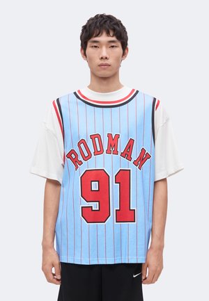 Joven con una camiseta de baloncesto azul con rayas rojas, "RODMAN" y el número 91 sobre una camiseta blanca.