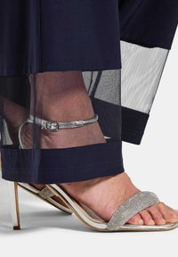 Marine kleding met transparante gaasdetails aan de zoom, gecombineerd met een zilverversierde hoge hak sandaal met enkelbandje.