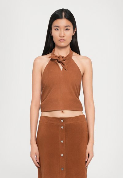 Bruine suède halter crop top met een geknoopte hals, voorzien van een sleutelgatdetail. Gecombineerd met een bijpassende midi-rok met zilveren knoopaccenten.