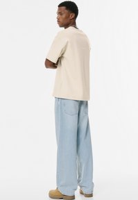 Beige kortærmet t-shirt med en afslappet pasform, parret med lyseblå vidde jeans. Chunky beige sko og metalnederdel synlige.