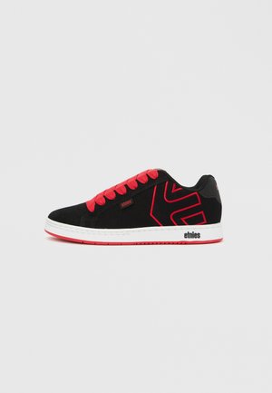 Zapatilla baja negra y roja con cordones rojos, suela blanca y diseño geométrico rojo en el lateral, con la marca "etnies" en la suela y la parte superior.
