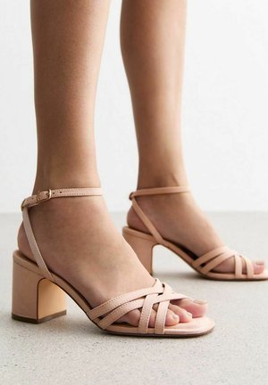 Roze hakken sandalen met gekruiste banden en een enkelgesp. Soepele textuur en een blokhak, met open tenen en een minimalistisch ontwerp.