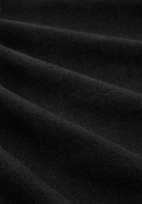 Černá tkanina s viditelnou jemnou strukturou a jemným leskem, splývající v jemných záhybech, zdůrazňující její neprůhlednou, hladkou kvalitu.