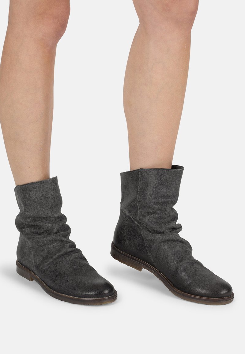 Botas de tobillo negras, con diseño desgarbado, fabricadas en suave ante, con punta redondeada y suela plana, que presentan un acabado texturizado y un diseño minimalista.