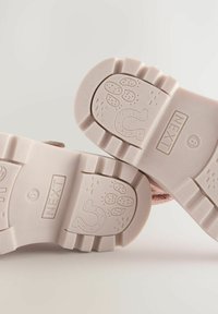 Plantillas de zapato de goma texturizadas en color rosa con patrones de relieve, incluyendo motivos juguetones y el texto "NEXT" y talla "6."