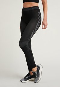 Sorte treningsleggings med høy midje, med teksturerte mønstre og grå chevron-detaljer langs siden. Kombinert med grå sneakers.