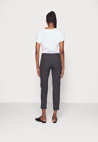 Damesoutfit met een plain wit t-shirt en donkergrijze broek tot de enkels met een decoratieve studded tailleband.