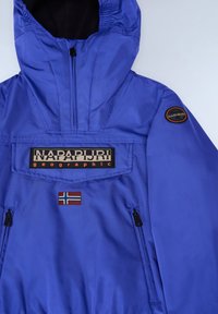 Fialový anorak vyrobený z hladkého, voděodolného materiálu. Obsahuje přední klopu s logem "NAPAPIJRI", detail norské vlajky a boční zipové kapsy.