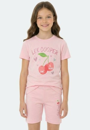 Fille portant un t-shirt rose Lee Cooper avec un motif de cerises et de cœurs, assorti à un short rose avec de petites cerises et le logo de la marque.