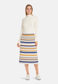 Long-sleeve white top with textured pattern, paired with a striped pleated midi skirt in blue, orange, and yellow. Worn with white shoes.