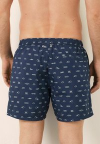 Marine zwemshorts met een patroon van lichtblauwe vissen en vissersknopen. Voorzien van een elastische tailleband met een koord en twee oogjes.
