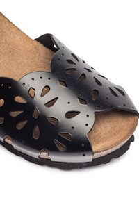Black leather sandal featuring cut-out floral designs, a cork footbed, and a textured rubber sole for grip and comfort.