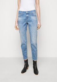 Jeans de mezclilla azul claro con un corte ajustado, diseño de cinco bolsillos y leve desvanecimiento. Cuentan con un cierre de botón y cremallera, combinados con botas negras hasta el tobillo.