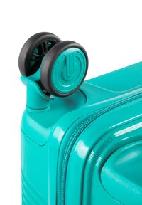 Valigia rigida turchese con finitura testurizzata, due ruote nere e manico arrotondato. Presenta un'apertura con zip per un facile accesso.