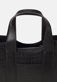 Mustakrokotettule nahkakassi sileäpintaisilla yksityiskohdilla ja kaksilla kahvoilla. Varustettu vetoketjullisella osastolla ja avoimella ylhäällä rakenteella.