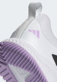 White athletic shoe featuring a textured upper, purple rubber outsole with ridges, and a pull tab at the heel. Black accent detail included.