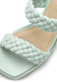 Mintgroene leren sandaal met drie gevlochten bandjes, een vierkante neus en een gladde beige binnenzool met subtiele textuur.