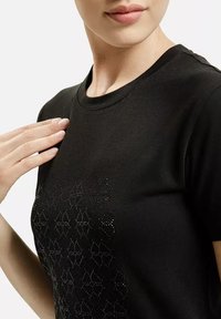 Czarna koszulka z krótkim rękawem, z teksturowanym wzorem małych, błyszczących akcentów na przodzie, z okrągłym dekoltem i miękkiego materiału.
