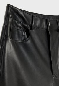 Gros plan sur un pantalon en cuir noir, mettant en valeur la poche avant, les passants de ceinture et les détails de la fermeture par bouton.