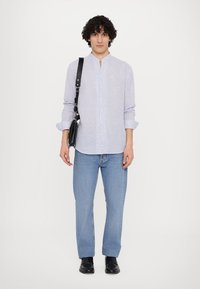 Prugasta srajca z gumbom v modri in beli barvi, v kombinaciji z svetlim denimom in črnimi čevlji, ob tem pa še črna torba čez ramo.