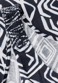 Svart- och vitt mönstrat tyg med geometriska former, med en smockad rem och en slät textur.