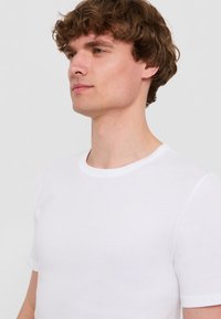 T-shirt bianco a maniche corte realizzato in morbido cotone, con colletto girocollo classico e texture liscia. Design semplice e pulito.