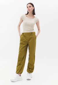 Beige tætsiddende top med korte ærmer parret med løstsiddende, olivengrønne bukser med snor i taljen. Hvide sneakers fuldender outfittet.