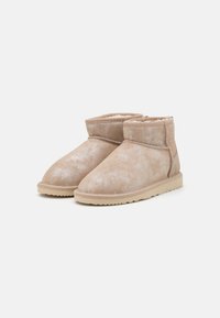 Bottes cheville en daim beige avec une finition texturée, dotées d'une doublure en fourrure douce et d'une semelle plate en caoutchouc. Le design présente des accents de couture minimalistes.