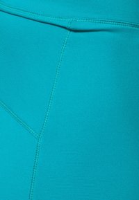 Leggings de sport teal en tissu lisse et extensible ; caractéristiques des coutures à plat et une taille haute avec une texture subtile.