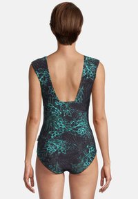 Maillot de bain noir avec un motif floral vert, design dos en V profond, manches courtes et tissu lisse, mettant en valeur la silhouette.