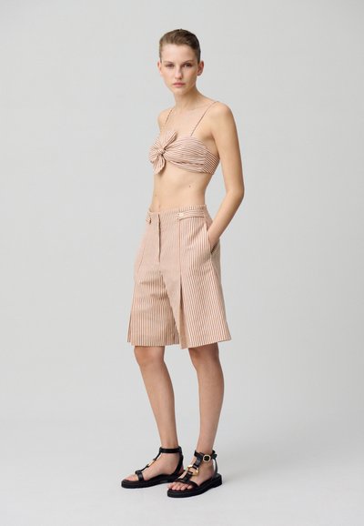 Conjunto a rayas de dos piezas que presenta un top anudado y pantalones cortos de pierna ancha en beige y óxido. Sandalias con correas negras y acentos dorados.