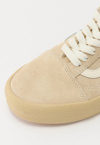 Beige mocka sneakers med vita snören, gummisula och krämfärgade detaljer. Rundad tå med ett strukturerat mönster på sulan.