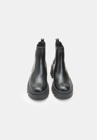 Melnas ādas Chelsea zābakus pāris ar biezajiem zolēm un vilkšanas cilpām, redzams no priekšpuses uz baltas fona.