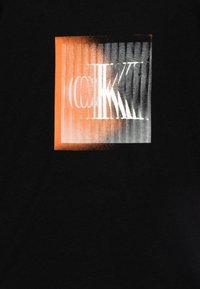 Schwarzes T-Shirt mit einem grafischen Druck in Orange- und Grautönen, das abstrakte Buchstaben und vertikale Linien fürTextur zeigt.