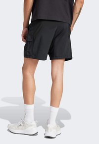 Black cargo shorts feature a side pocket, made from a smooth material. Paired with white socks and light sneakers.