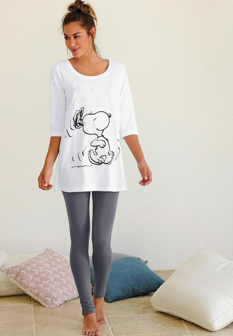 White tunic with a Snoopy print and stars, paired with grey leggings. The tunic has a round neckline and three-quarter sleeves.