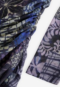 Gros plan d’un tissu avec des motifs floraux et géométriques abstraits bleu, violet et noir, montrant des sections froncées et plates.