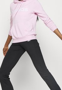 Rosa Kapuzenpullover mit weißem "adidas"-Logo, Vordertasche, kombiniert mit schwarzen Sporthosen mit kleinem Logo an der Hüfte; glatter Stoff, figurbetontes Design.