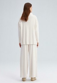Conjunto de loungewear ligero y color crema con textura acanalada; cuenta con una parte superior holgada con cuello y pantalones de pierna ancha.