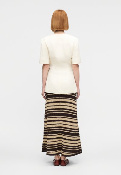 Εκρού εφαρμοστό σακάκι με κοντά μανίκια, συνδυασμένο με μακριά πλεκτή φούστα σε ρίγες σε καφέ και μπεζ αποχρώσεις, φορεμένο με καφέ παπούτσια.