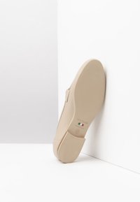 Scarpa in pelle beige con superficie liscia, caratterizzata da punta arrotondata e tacco basso a blocco. Include un marchio in rilievo sulla suola.