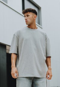 Šedé oversized tričko z jemné bavlněné směsi s kulatým výstřihem a krátkými, spadlými rukávy. Nosené s světle modrými džínami.