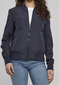 Navy bomber jacket made of smooth fabric, featuring a front zipper, ribbed cuffs, and hem, with side pockets and a classic silhouette.