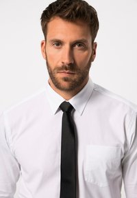 Camisa blanca con un bolsillo en el frontal y corbata negra. La tela parece suave y nítida, mostrando una apariencia clásica y formal.