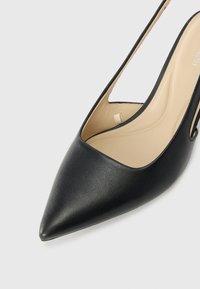 Tacco alto in pelle nera con punta affusolata e design slingback. Presenta una texture liscia e una soletta di colore chiaro.