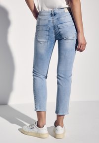 Jeans skinny de mezclilla azul claro con una cintura de media altura, dos bolsillos traseros y un corte ajustado, combinados con zapatillas blancas.