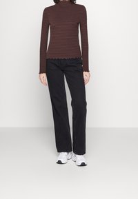 Brun och vinröd randig långärmad topp med vågiga kanter, kombinerad med svarta raka jeans och vita sneakers.