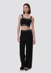 Zwarte crop top met decoratieve gouden accenten en wijde broek met een vergelijkbare afwerking. Glanzende spitse schoenen maken de outfit compleet.